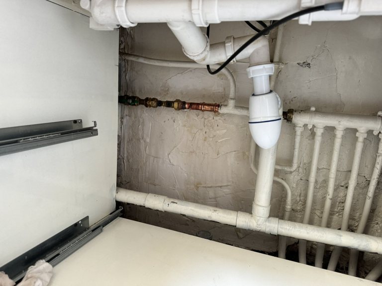 Raccords en cuivre et robinetterie à côté du siphon sous un évier.