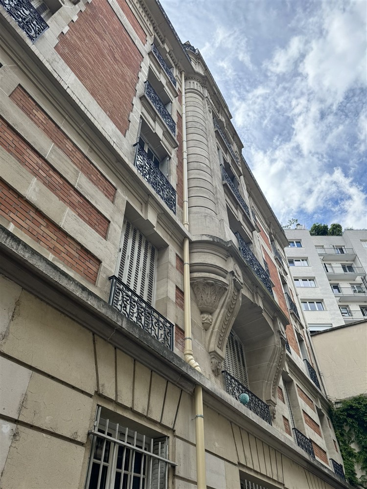 Descente beige longeant une façade en pierre et en brique.